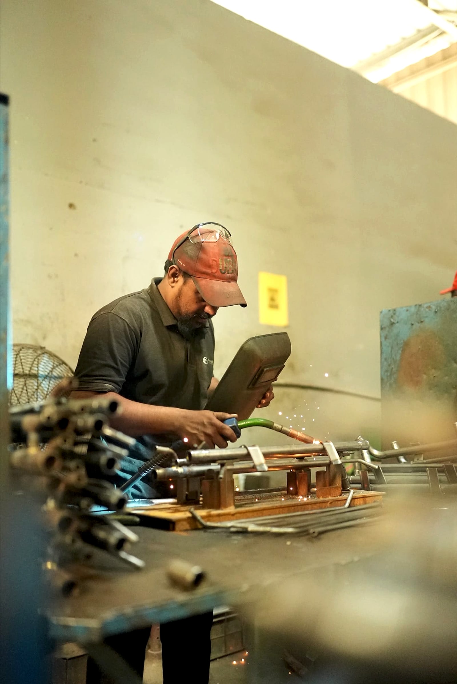 Welder in a cap and safety glasses MIG welding a pipe assembly on a fixture