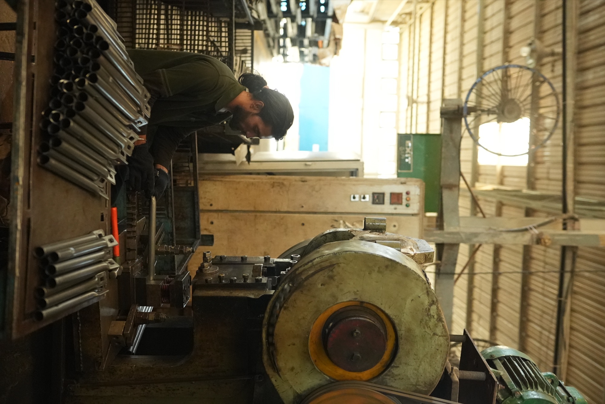 Operator forming the ends of steel tubes on a power press, with finished tubes stacked on the table