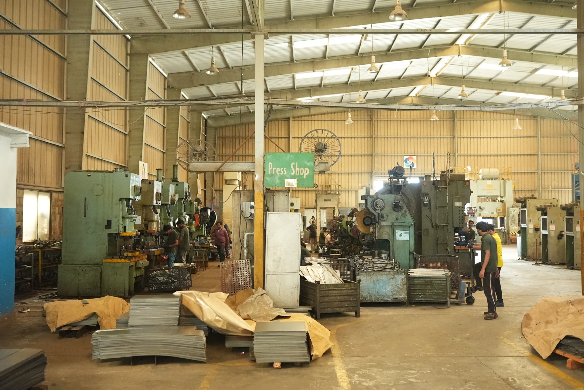 Wide view of the press shop hall with rows of presses, operators and stacks of sheet metal blanks