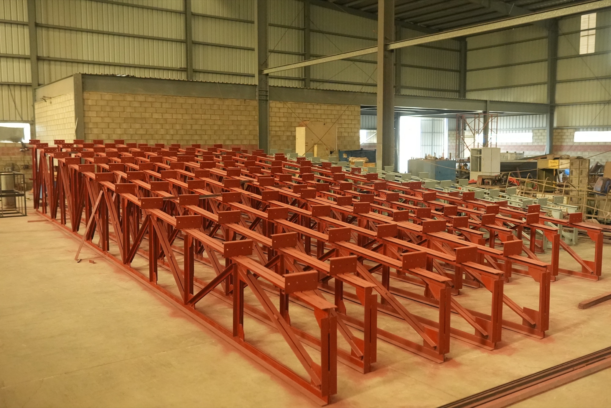 Rows of welded steel frames finished in red primer on the shop floor