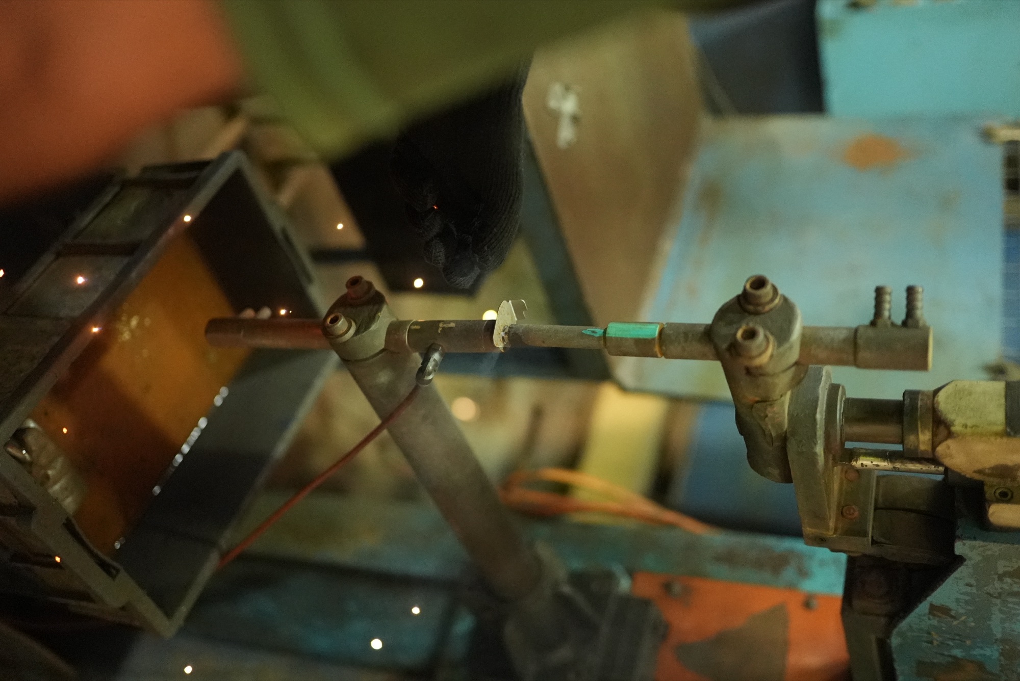 Gloved operator spot welding a bracket between the electrodes of a pedestal welder