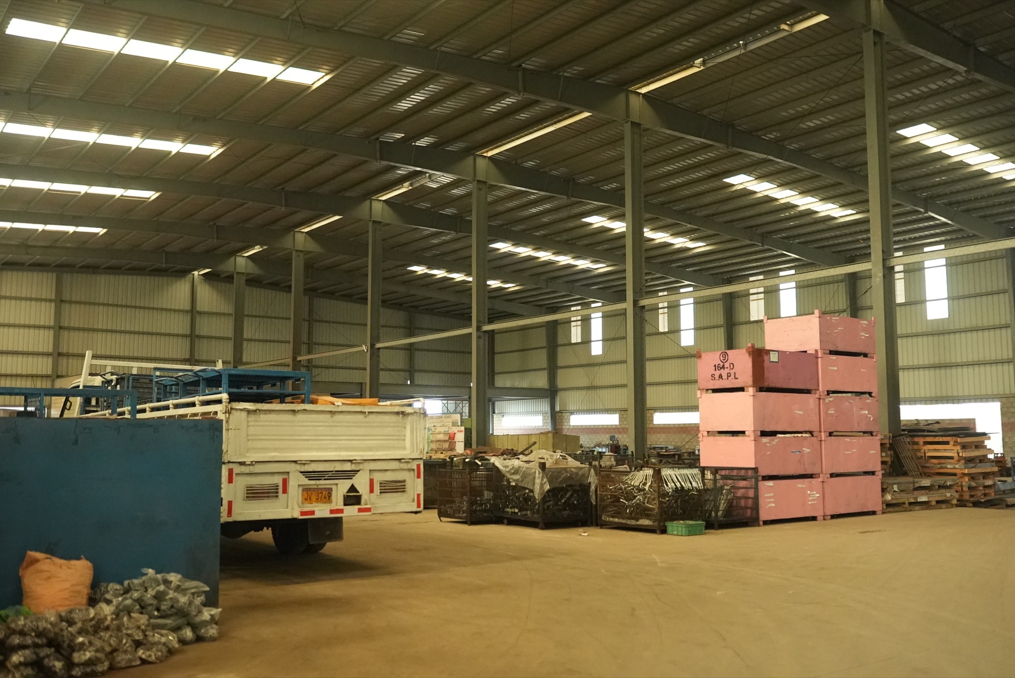 Warehouse bay with stacked SAPL part bins, wire cages of formed parts and a delivery truck